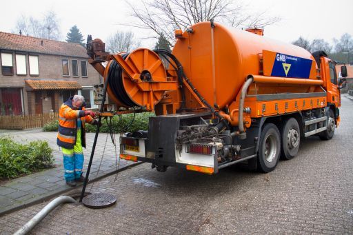 Man begeleidt vanaf een truck een slang het riool in voor een reiniging
